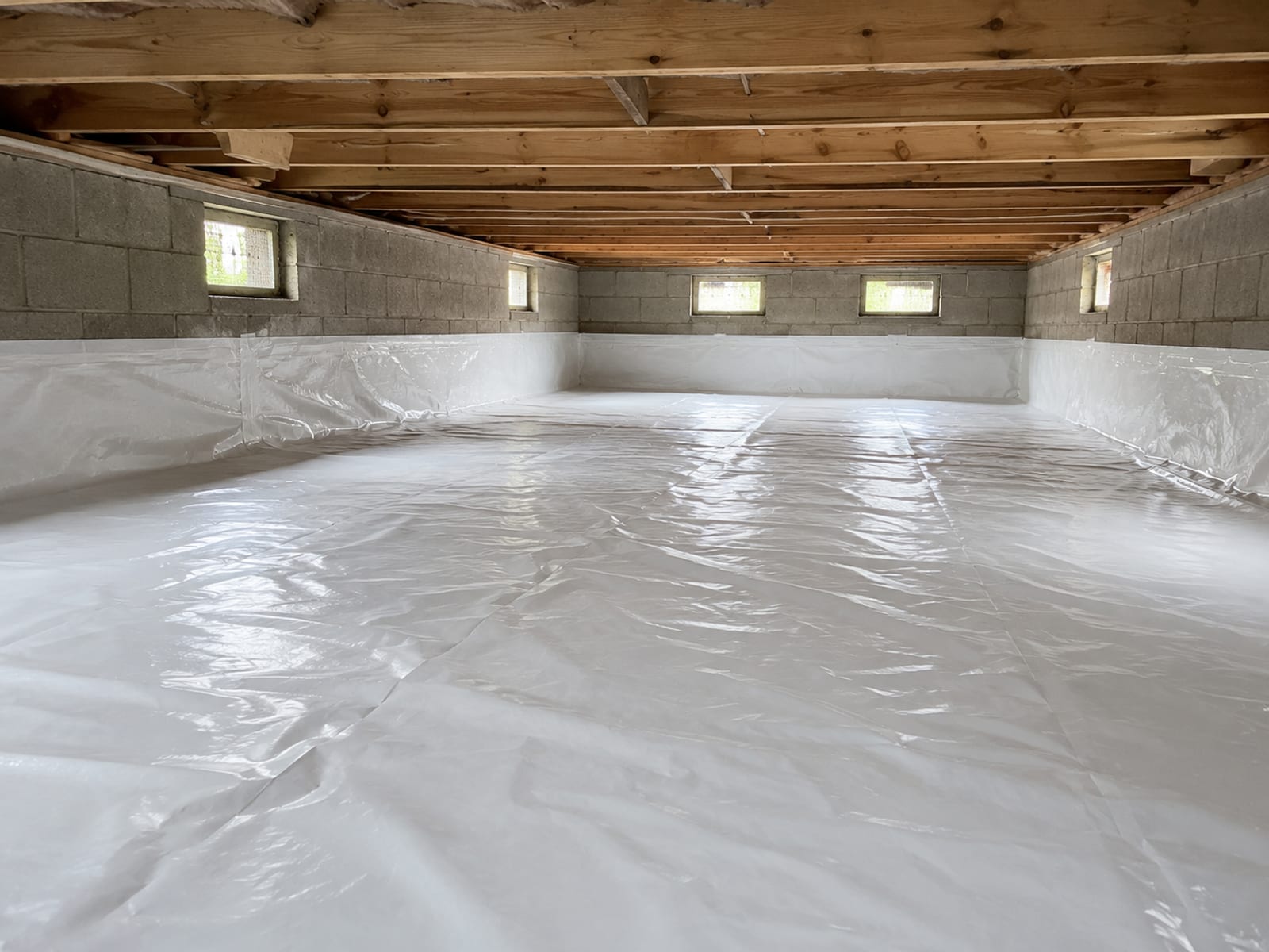 Finished excavated crawl space beneath a New England colonial home with a clean level soil floor, new vapor barrier sheeting, and open foundation vents allowing airflow