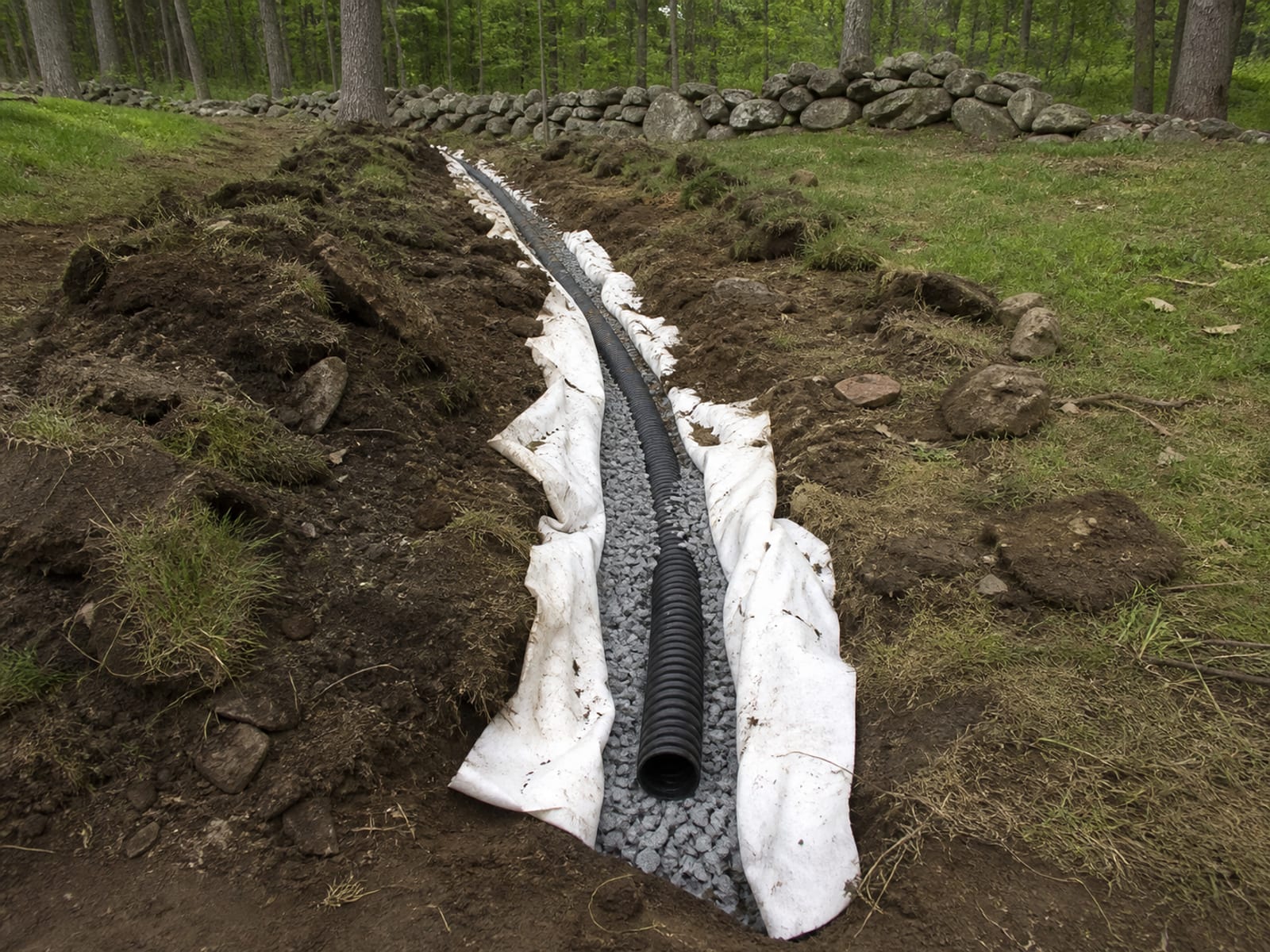 Open drainage trench with perforated pipe bedded in washed stone and filter fabric folded back along both sides of the excavation