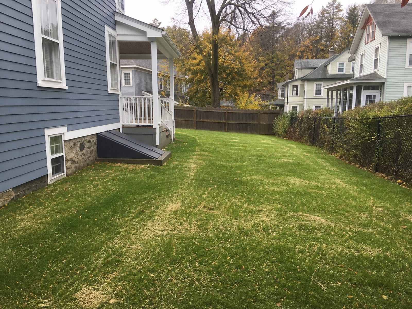 Restored residential lawn after drainage work, with fresh topsoil and seed over the backfilled trench line and a clean surface grade falling away from the house