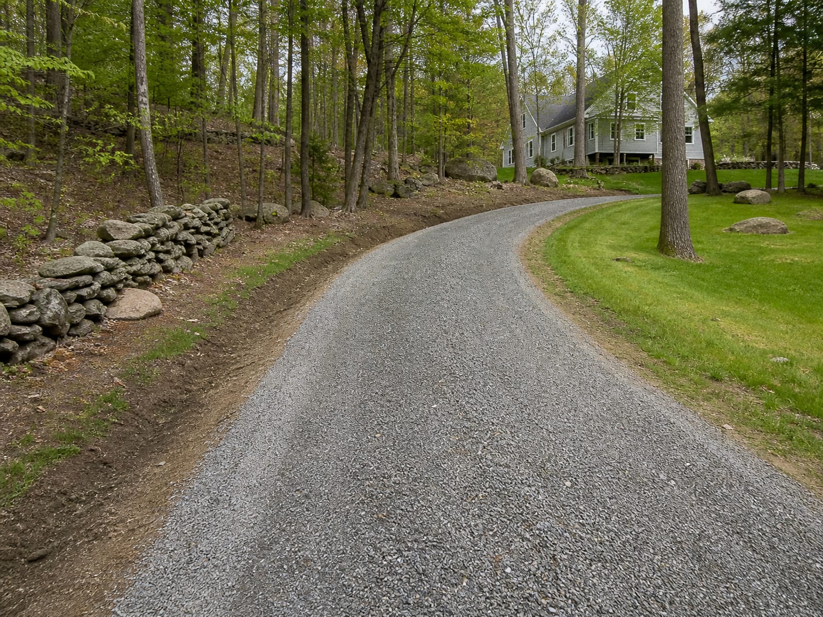 Rebuilt gravel driveway with a restored crown shedding to both shoulders, compacted surface, and a clear ditch line along one side