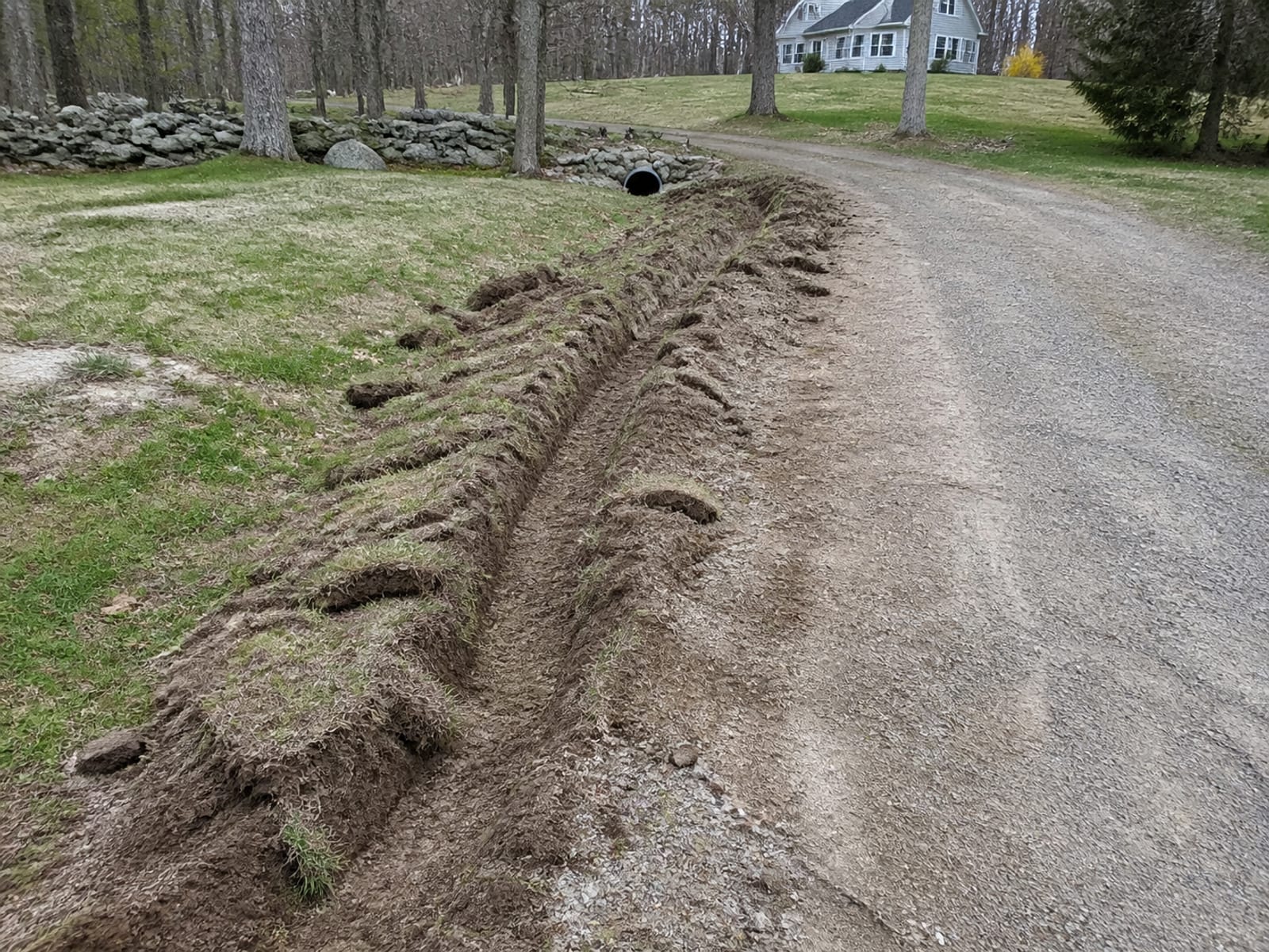 Shallow ditch running alongside a gravel driveway to a stone protected culvert outlet at a low point in the slope