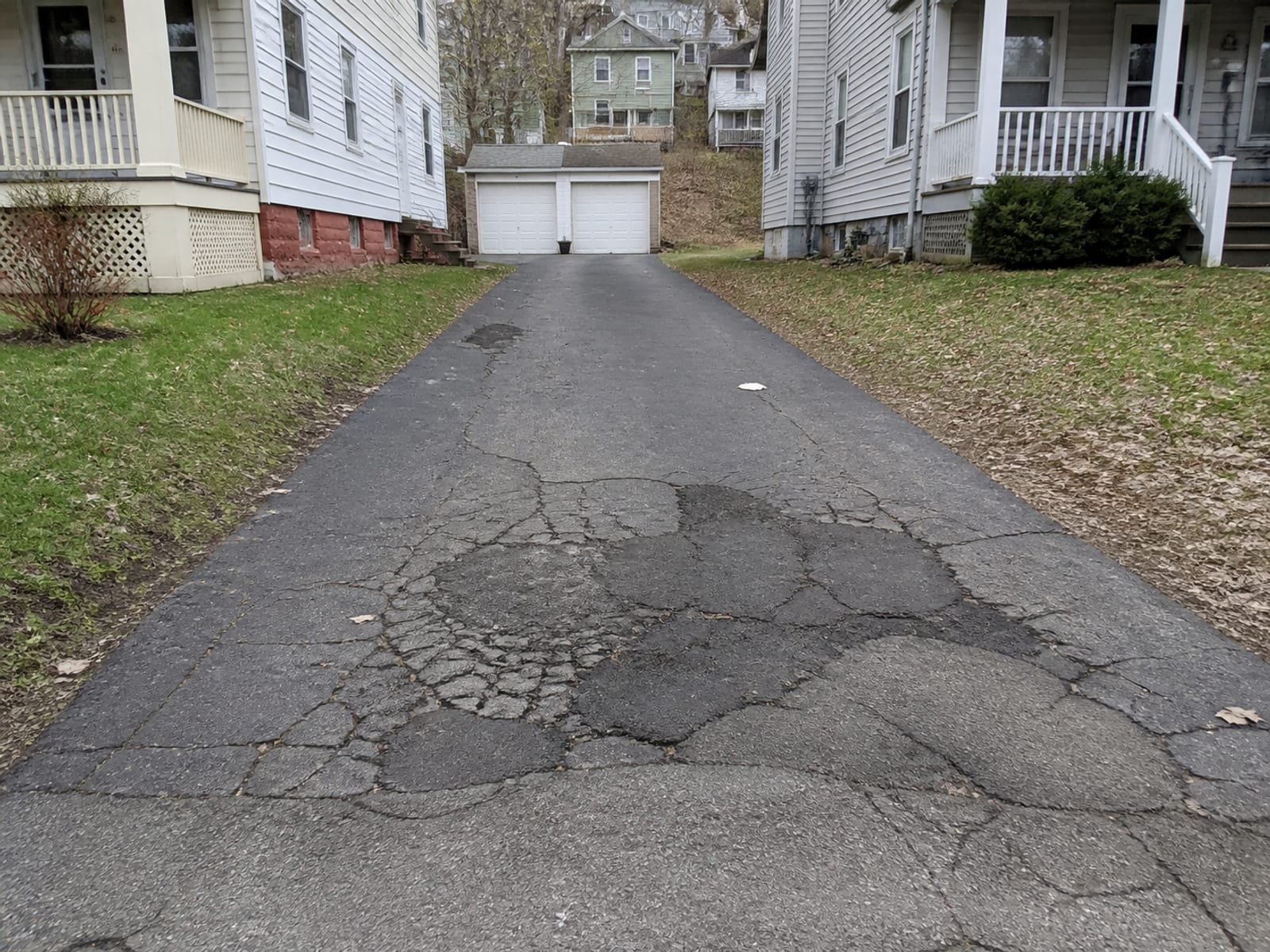 Residential asphalt driveway with a settled depression and cracking concentrated in one area, showing repeated patch repairs over the same spot