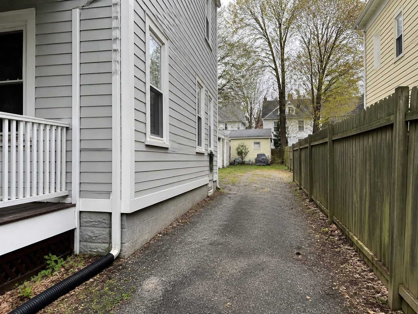 Narrow side access route between a residential property line and a house on a compact urban lot, with a driveway leading to a small back yard work area