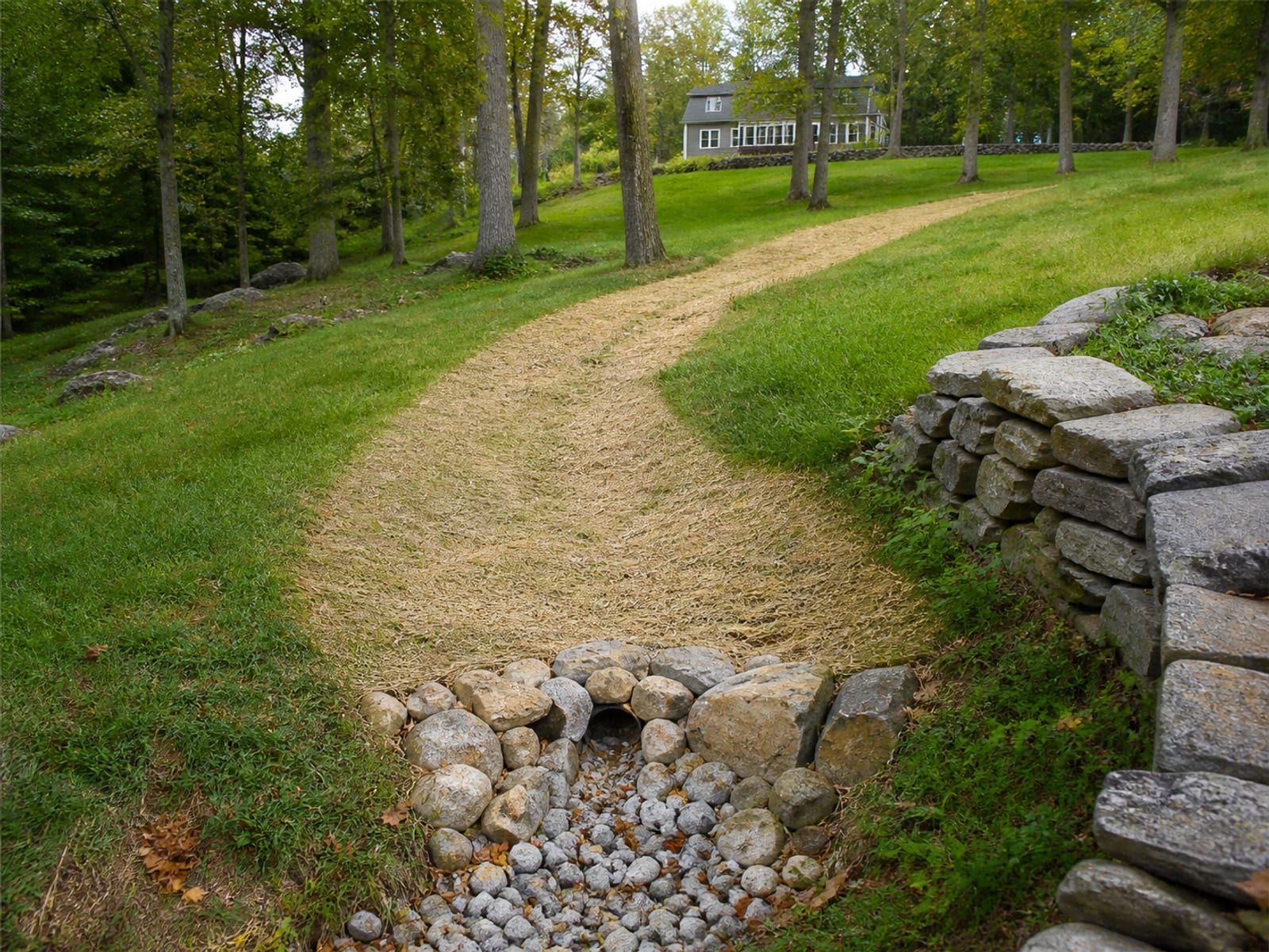 Completed grass lined swale across a residential slope with stone at the outlet and freshly seeded soil under straw mulch