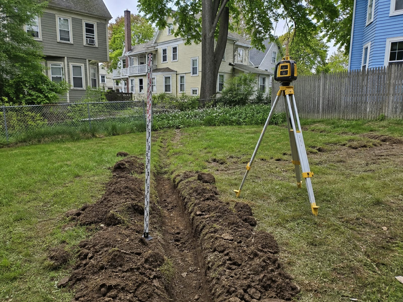 Survey grade rod and laser level set up on a residential lawn to check existing elevations before regrading work begins