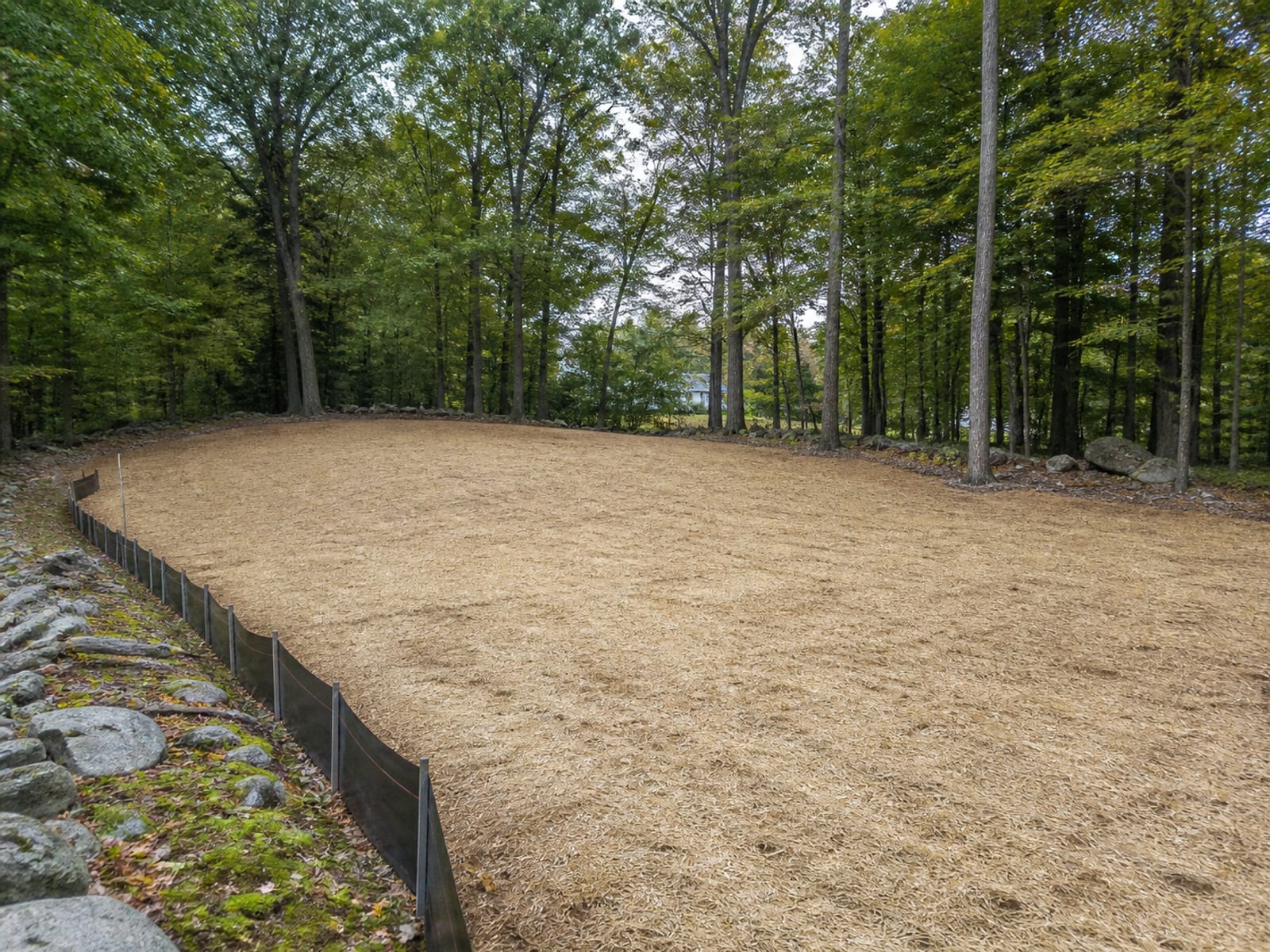 Newly cleared and rough graded opening in woodland with straw mulch over seeded soil and a silt fence along the downhill edge