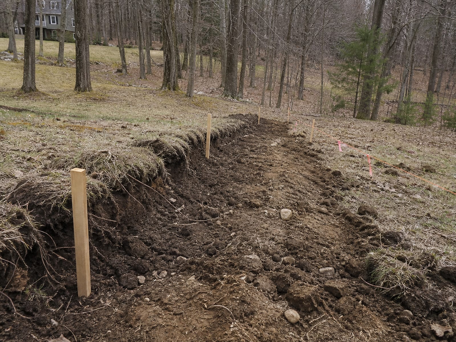 Grade stakes marking a planned level area on a slope, with the cut line marked into the bank on the high side and the fill limit flagged below