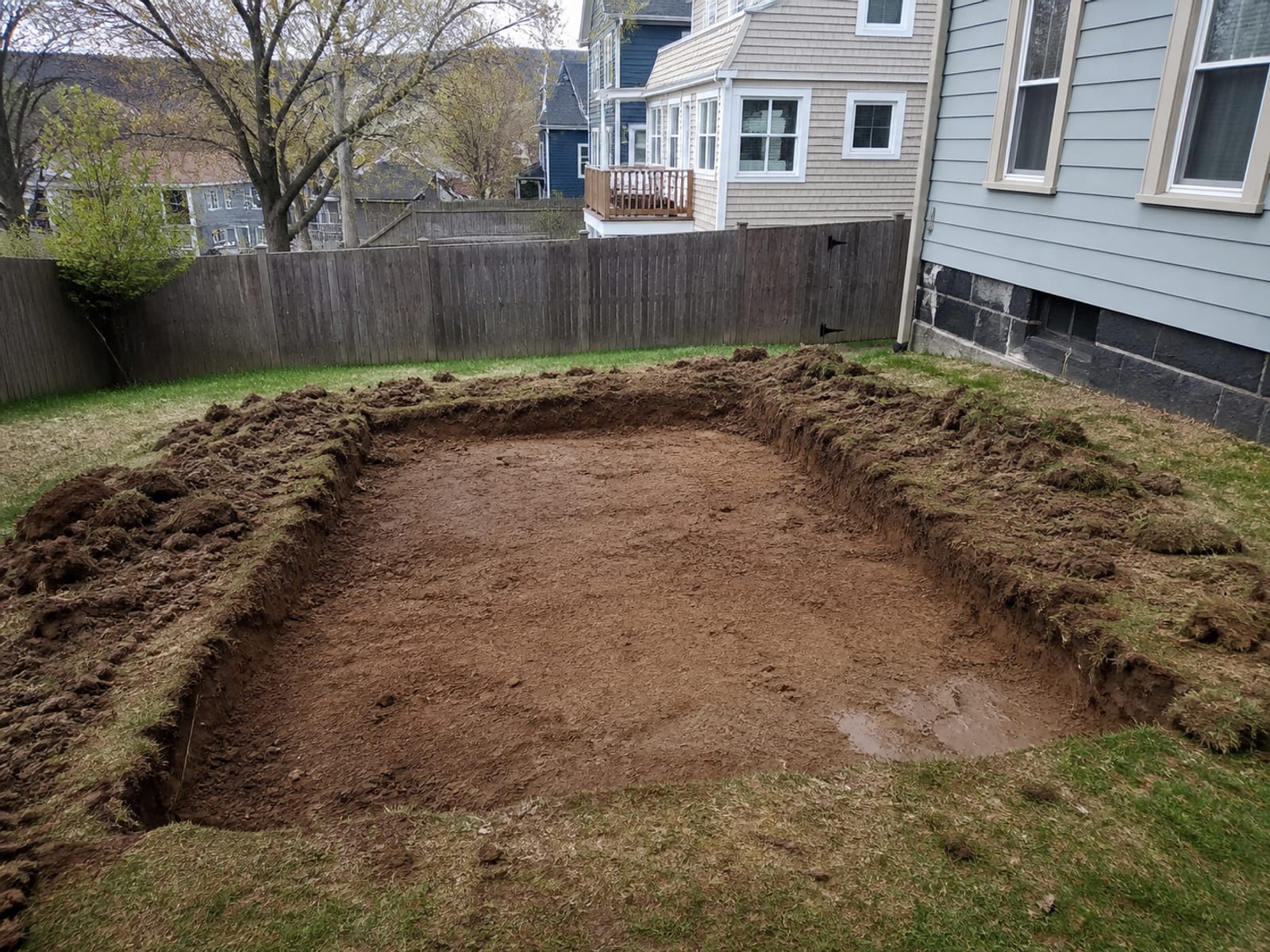 Excavated patio area on a compact residential lot with the subgrade shaped and a soft damp patch visible in one corner