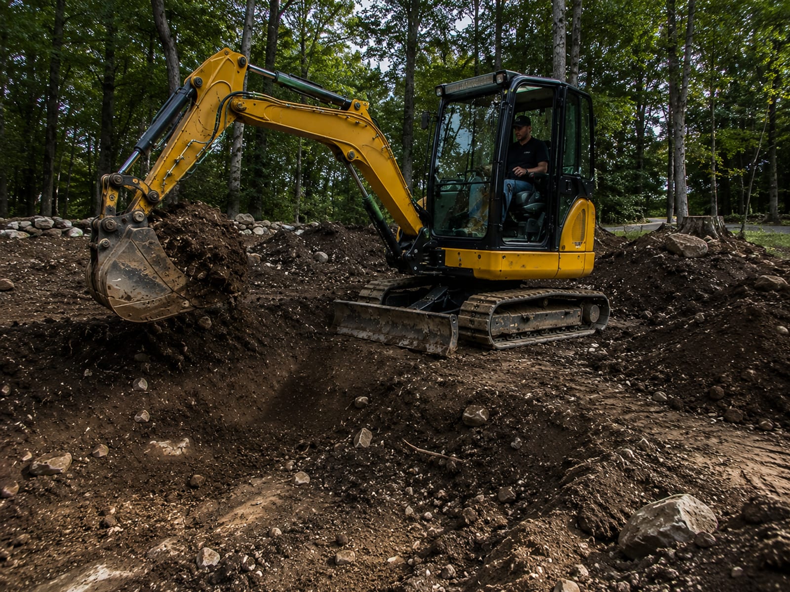 Compact yellow tracked excavator actively digging and loading spoil on a residential site preparation job in Connecticut
