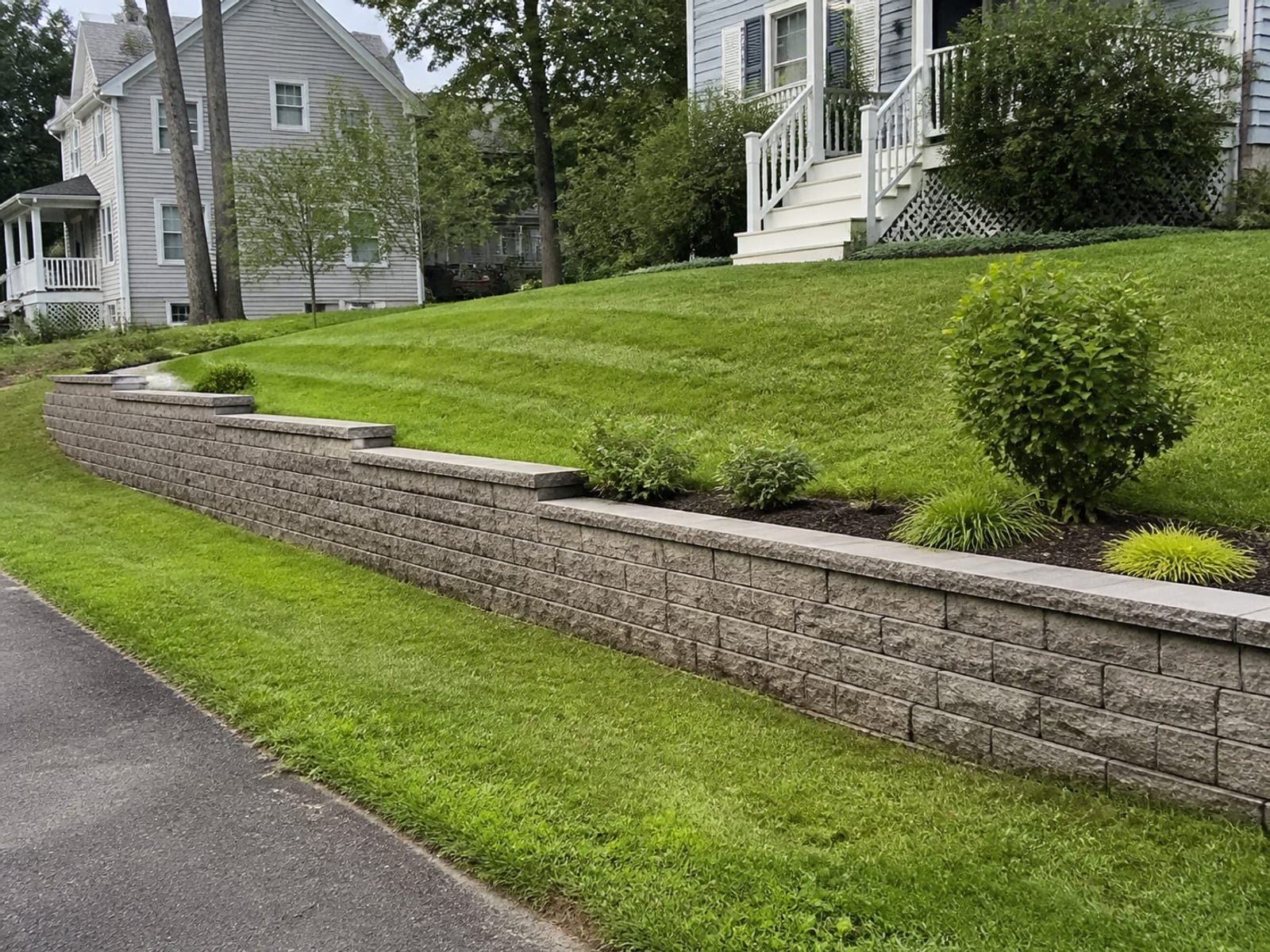 Completed segmental block retaining wall on a residential slope with level courses, restored grade above and below, and surface water directed away from the backfill