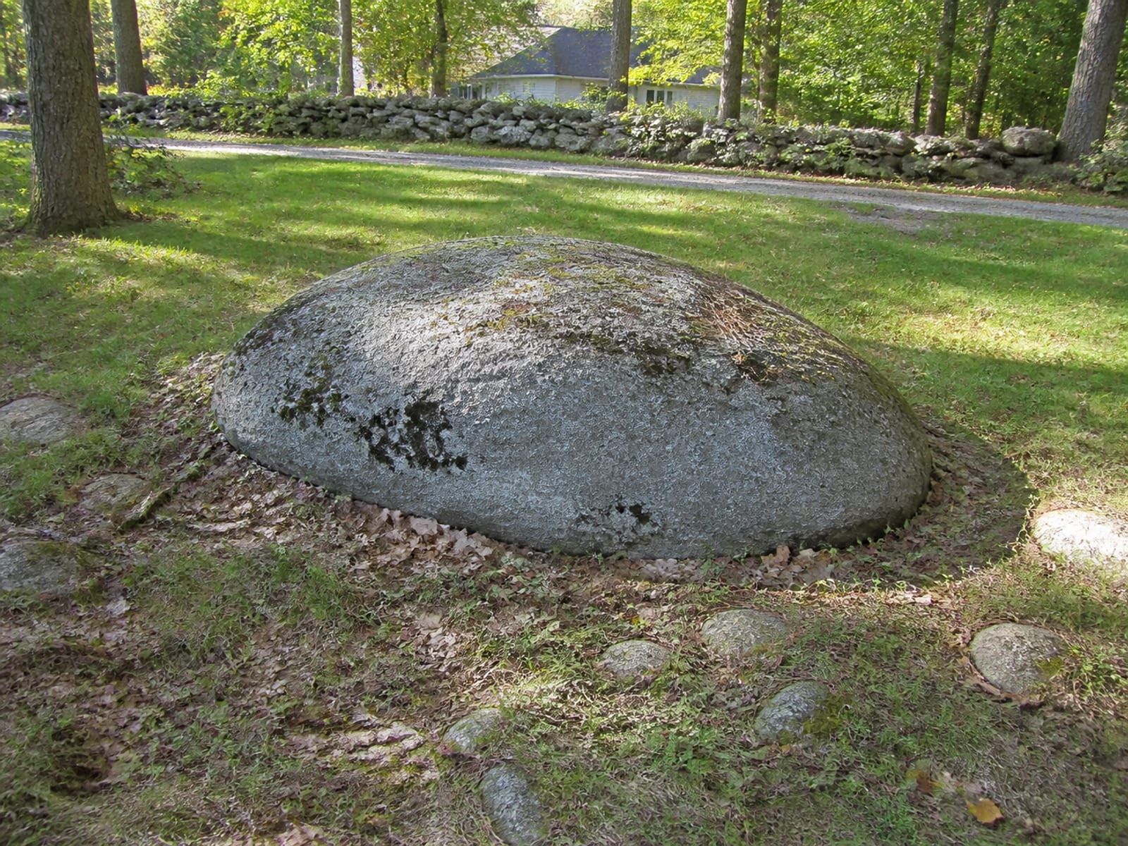 Large boulder partly exposed in the bottom of an open excavation on a rural lot, with stony till visible in the cut face around it