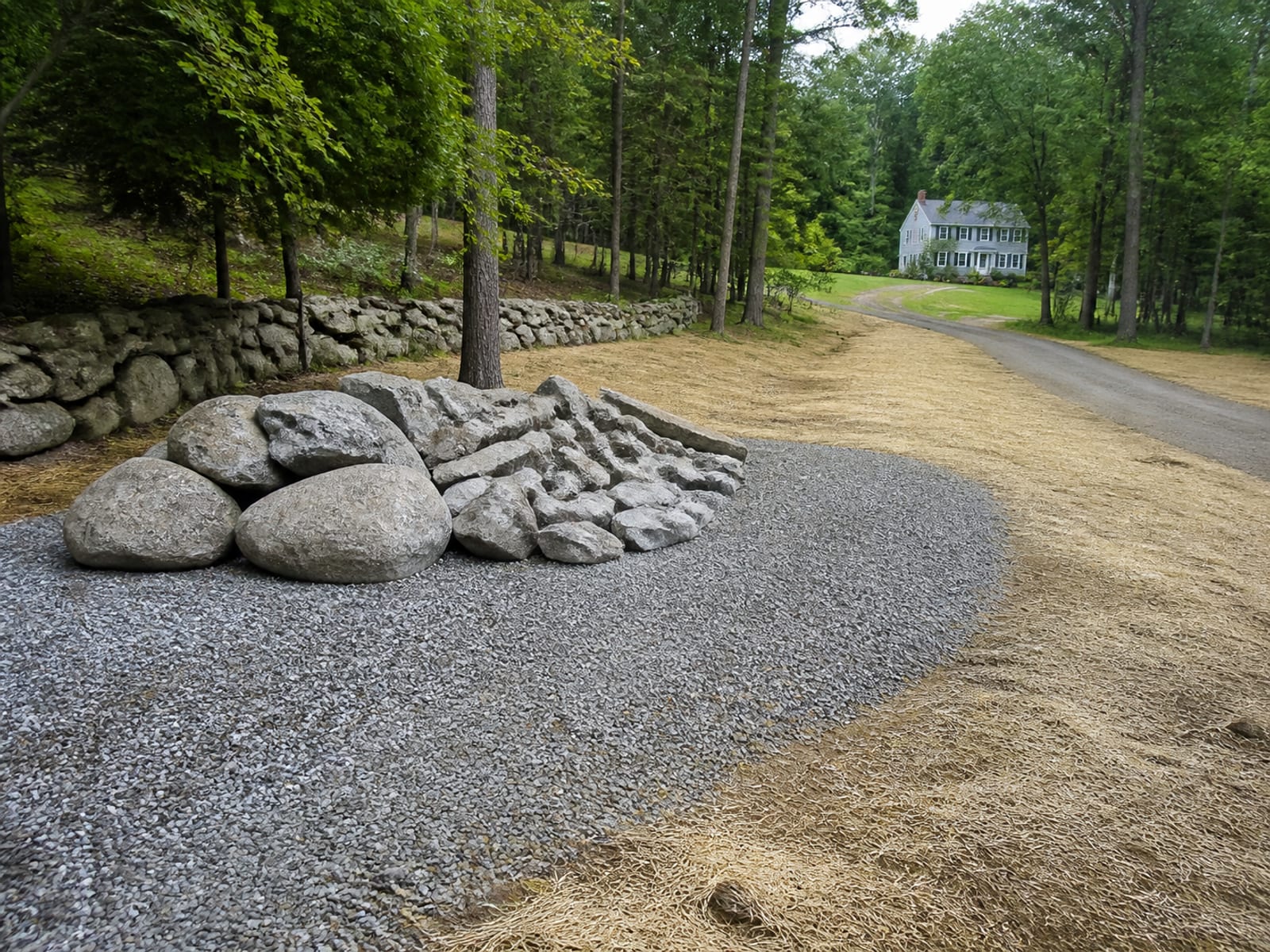 Excavated boulders and broken rock set aside in a stockpile at the edge of a rural work area, clear of the open excavation