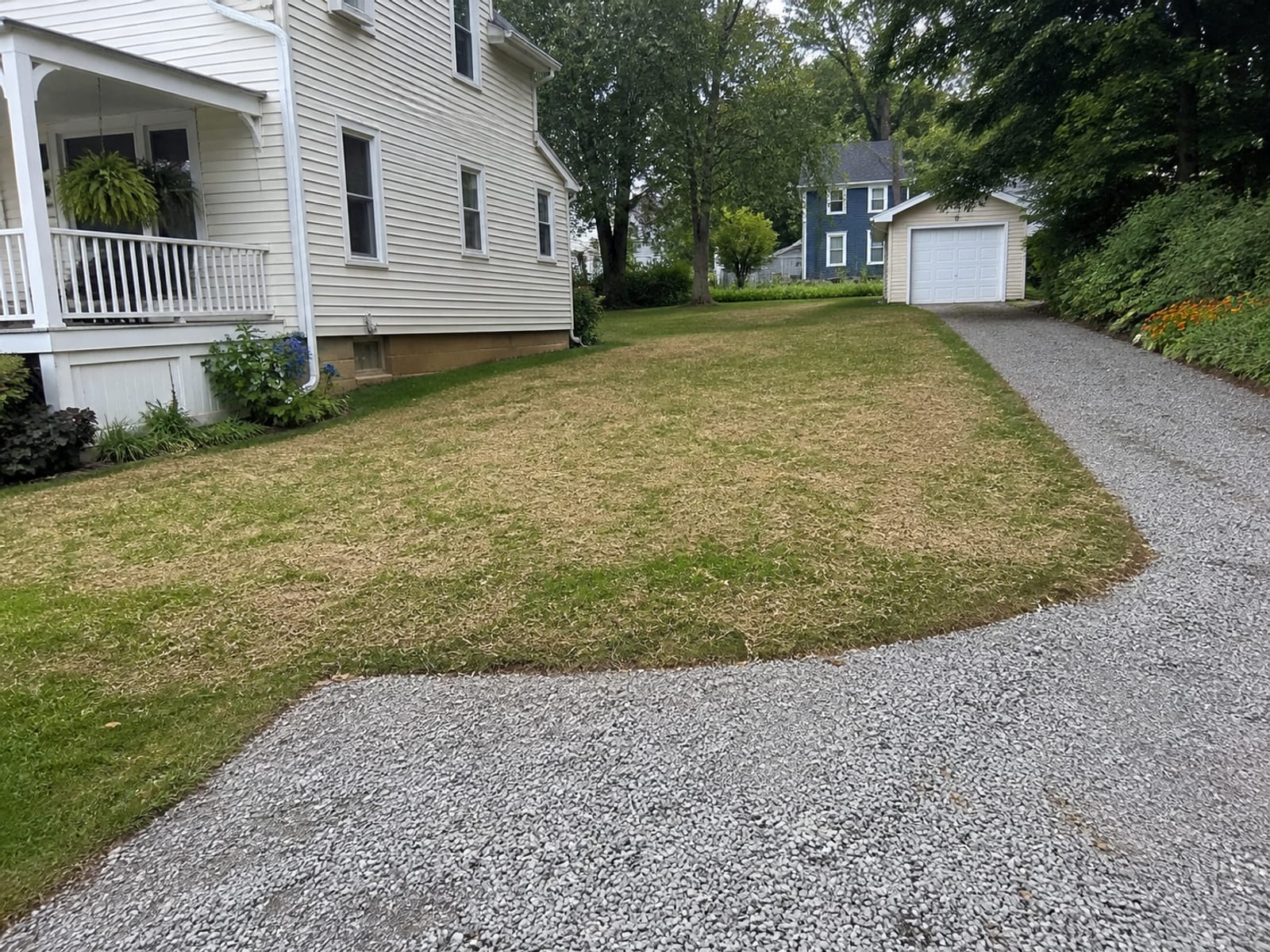 Completed excavation backfilled and brought to grade on a small urban lot, with the driveway edge and lawn restored where equipment had crossed