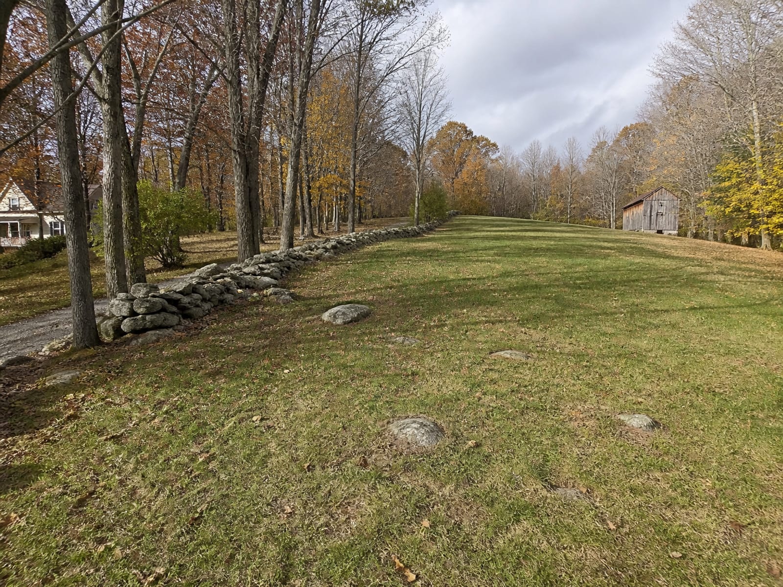 Long open rural lot with a wooded edge and a gentle rise, showing the ground a utility route would have to cross between a house and an outbuilding