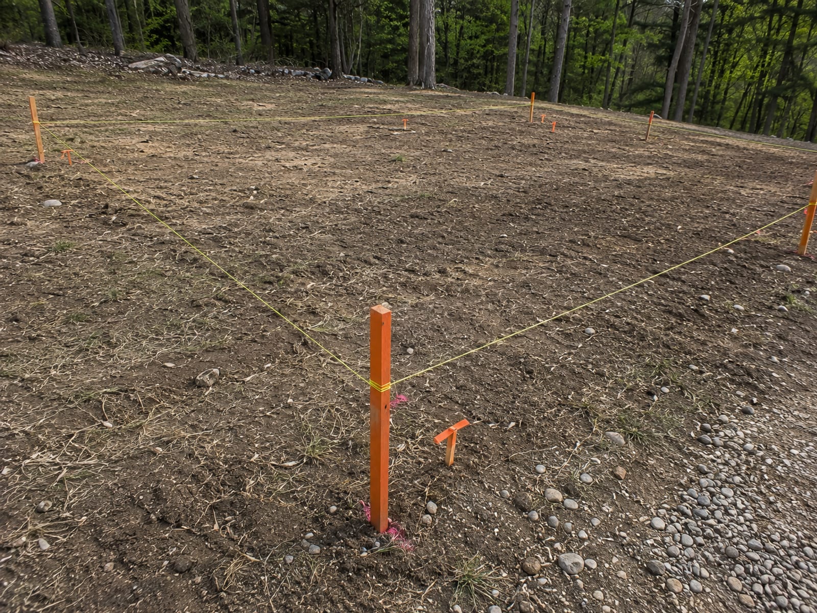Orange survey stakes and neon string lines marking a rectangular foundation footprint on a cleared residential lot in Connecticut before excavation begins