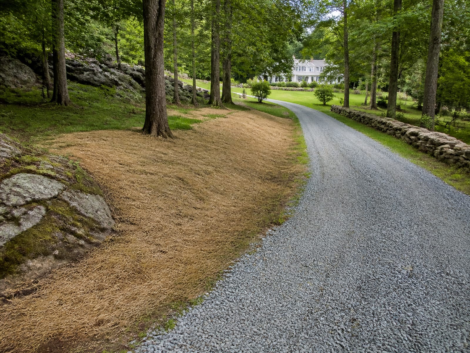 Rural driveway regraded and raked smooth after equipment traffic, with the work area backfilled, seeded, and straw covered nearby