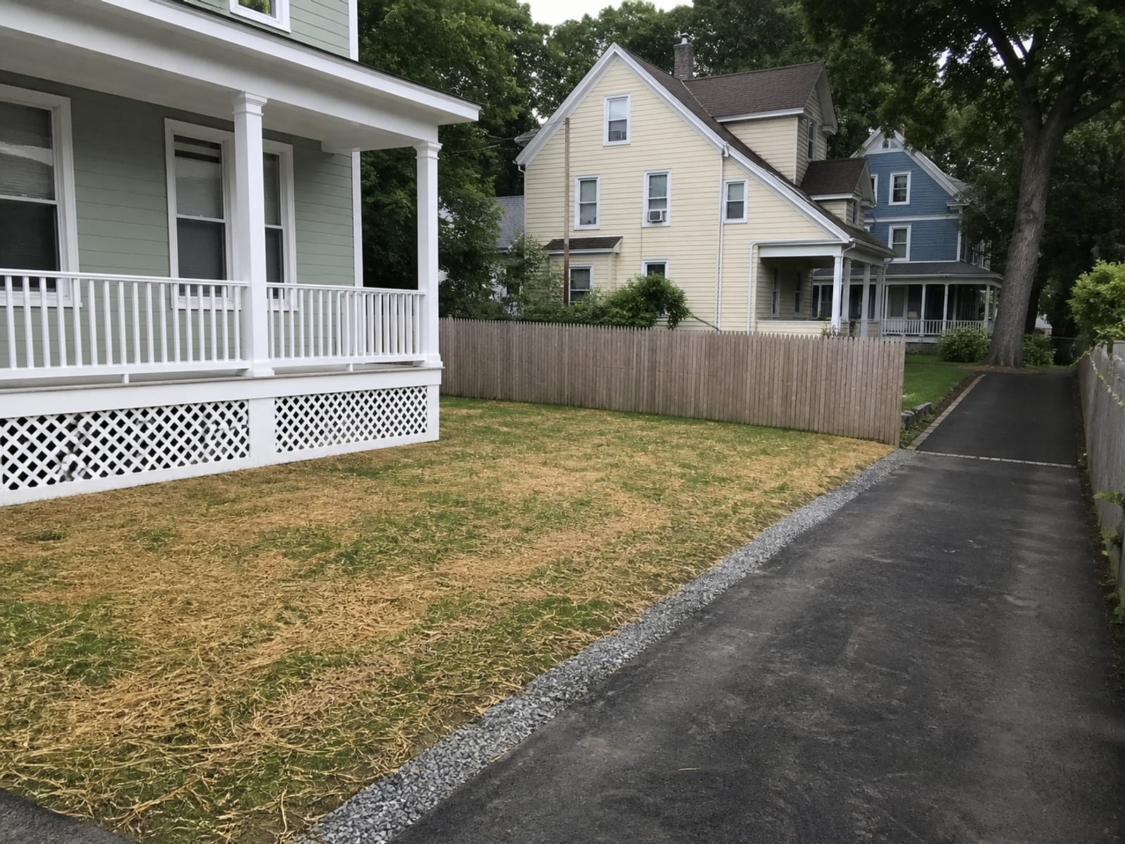 Completed work area backfilled and graded on a small urban lot, with the lawn repaired, the driveway clean, and the fence back in place