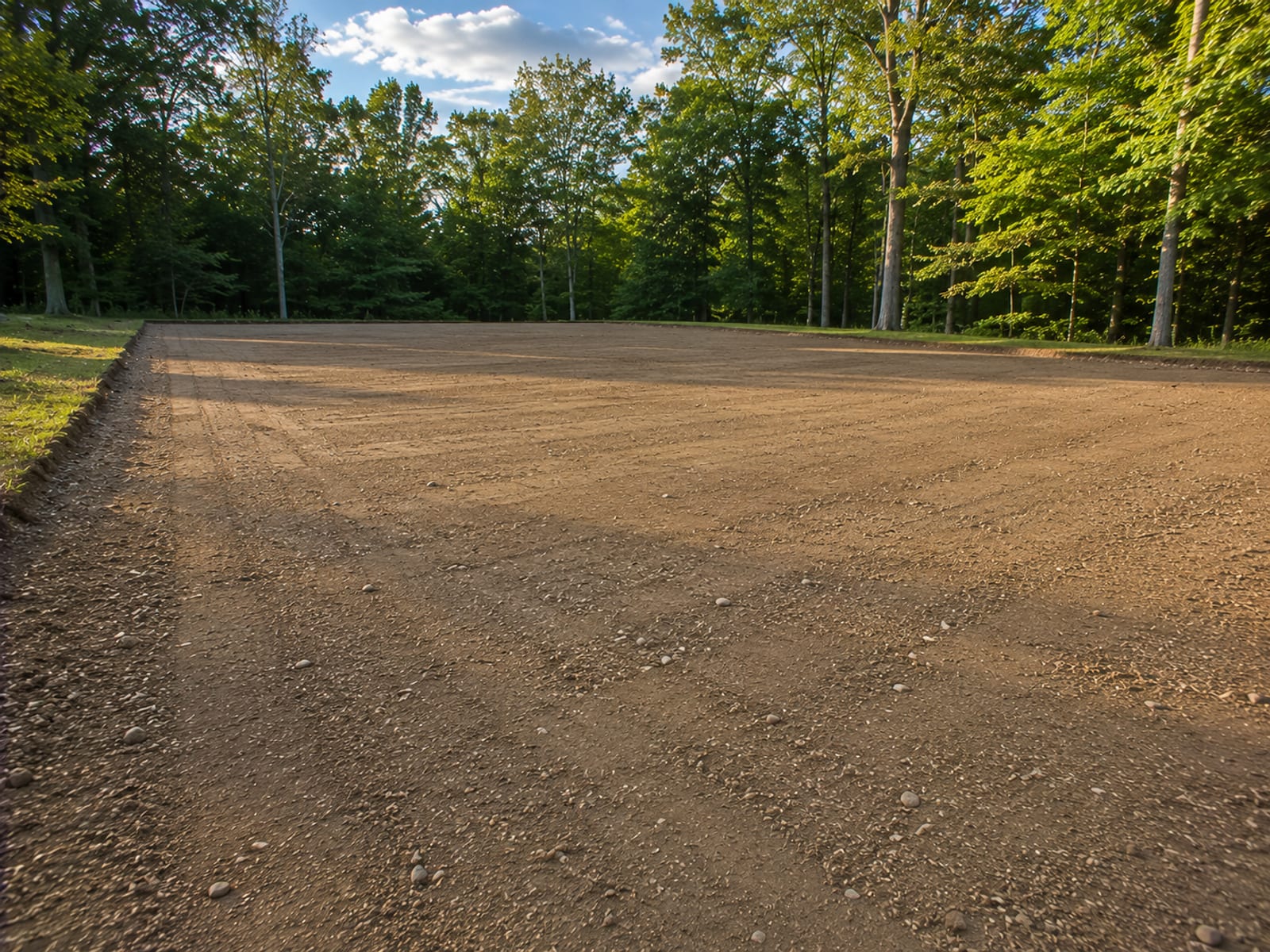 Smoothly graded residential lot with compacted level earth and clean edges ready for construction against a backdrop of mature Connecticut trees