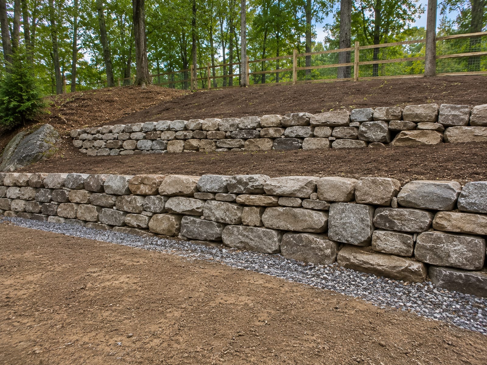 Newly constructed dry-stacked stone retaining wall terracing a sloped residential yard in Ansonia CT