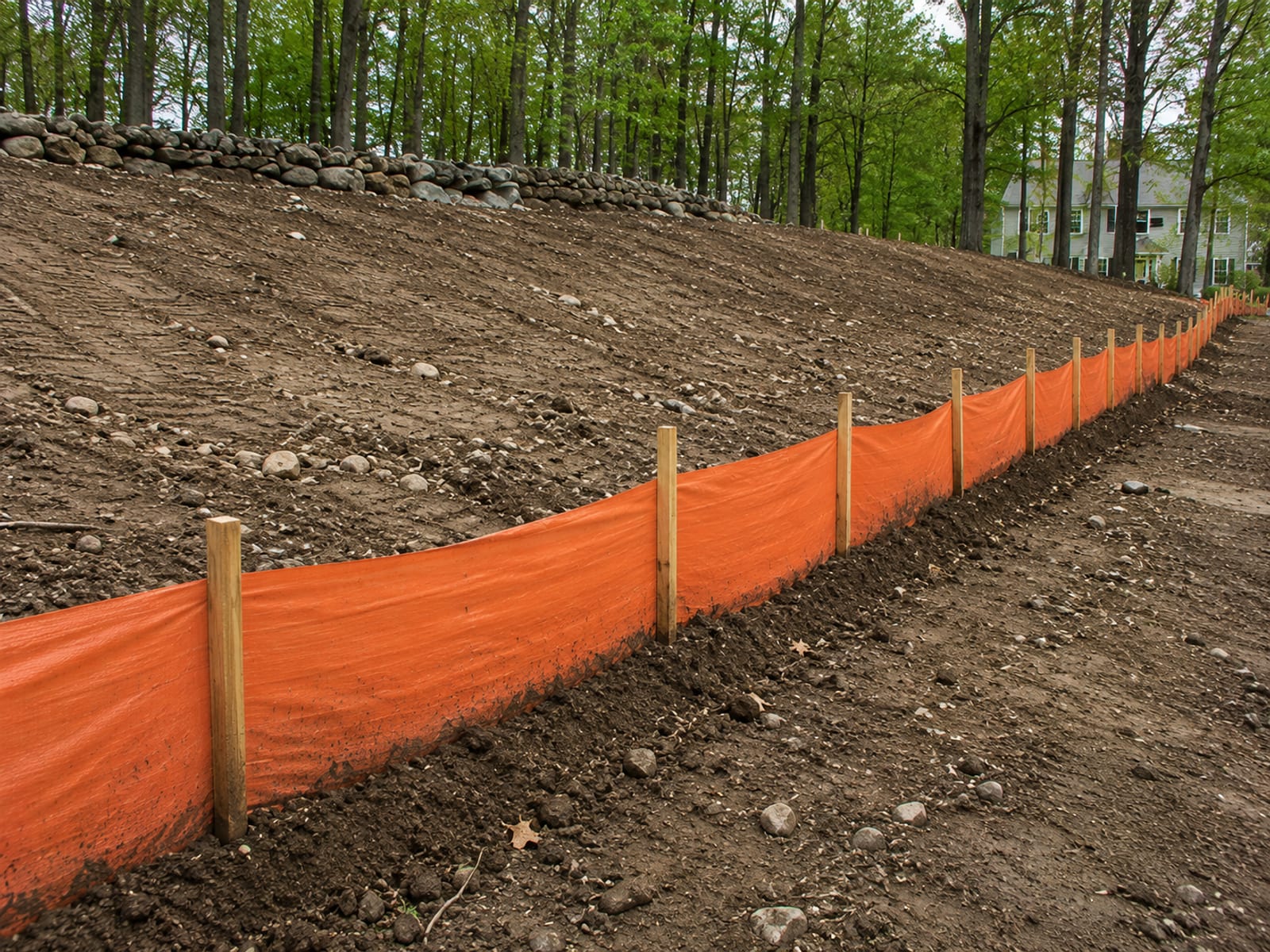 Silt fence erosion control barrier staked along a freshly graded slope on a residential excavation site in Connecticut