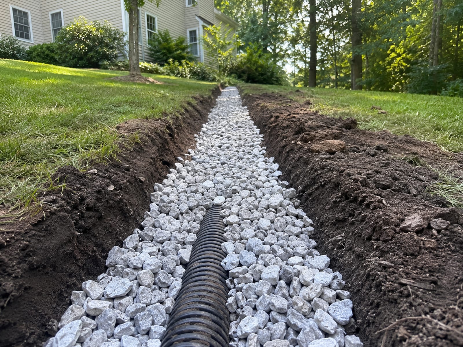 Completed French drain installation along a sloped residential yard in western Connecticut with gravel trench and perforated pipe visible