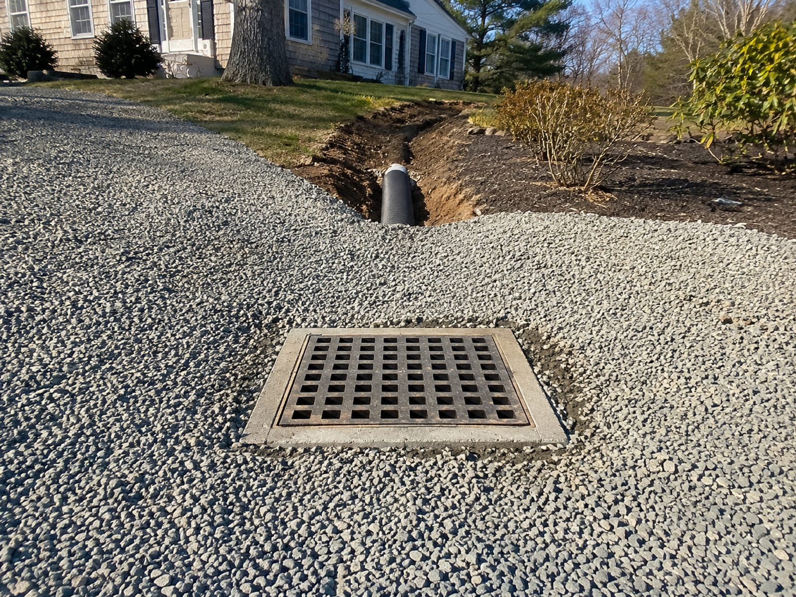 Concrete catch basin inlet set flush into a gravel driveway on a residential property in western Connecticut