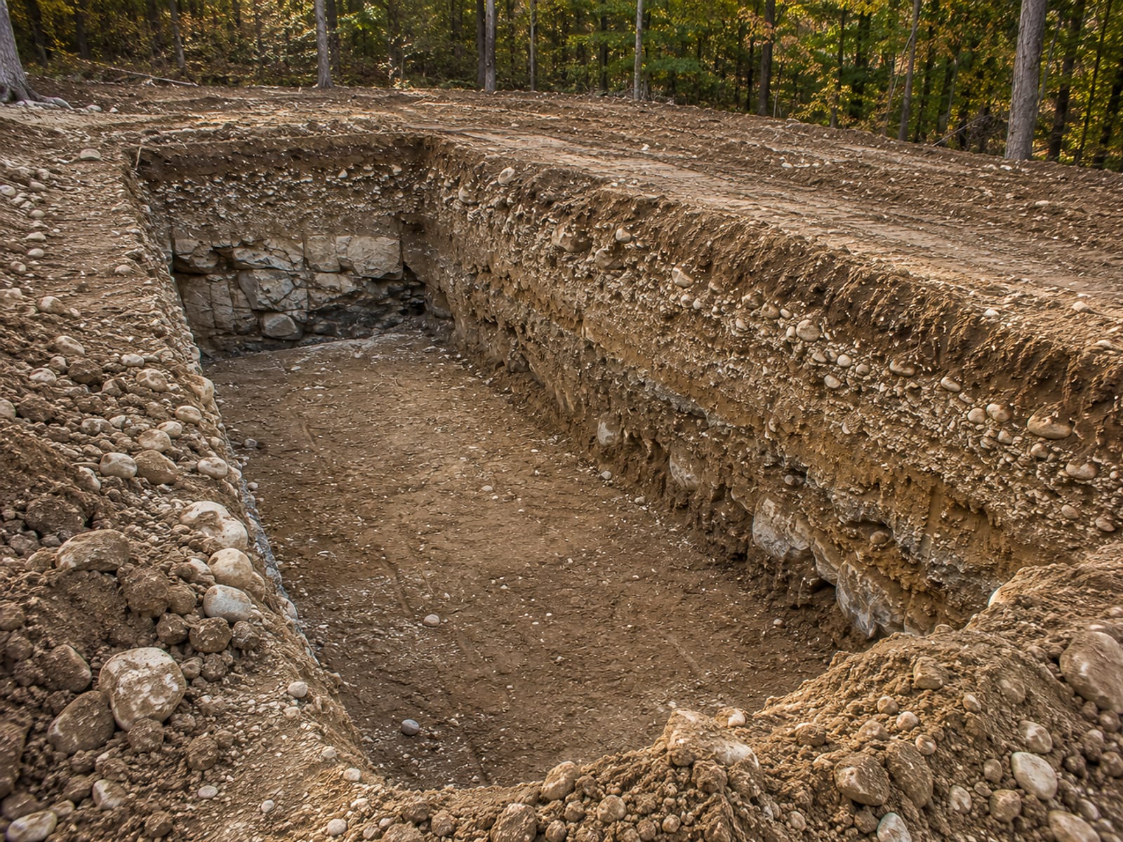 Deep excavated trench cut into rocky Connecticut soil exposing ledge rock and glacial till layers