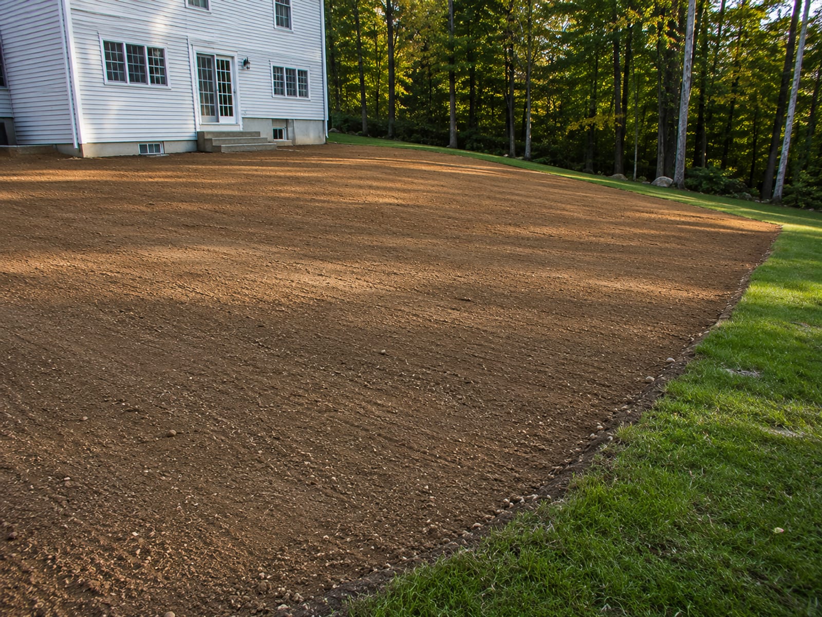 Smoothly finish-graded residential backyard with gentle slope away from a colonial home foundation in Connecticut