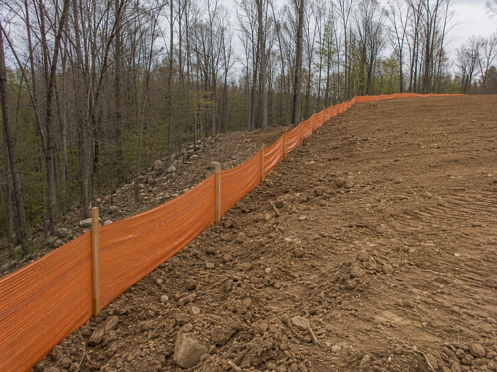 Silt fence installation along a freshly graded slope on a wooded residential lot in Connecticut
