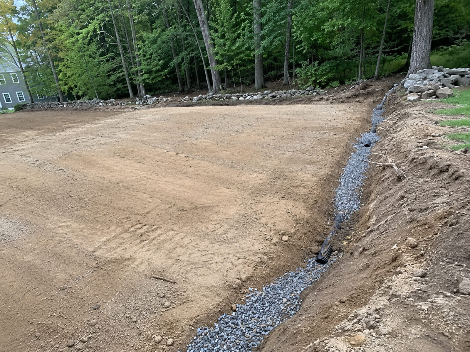 Freshly graded level building pad with a French drain trench cut along the slope edge on a Connecticut residential property