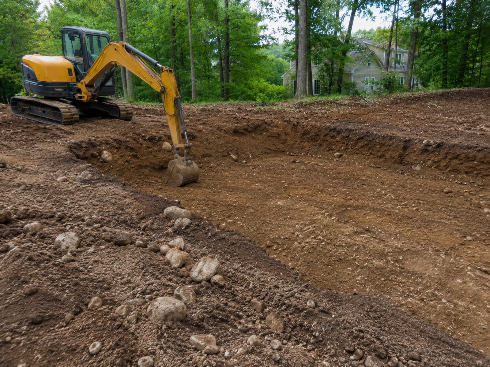 Compact yellow tracked excavator digging a wide foundation trench on a residential lot in Connecticut