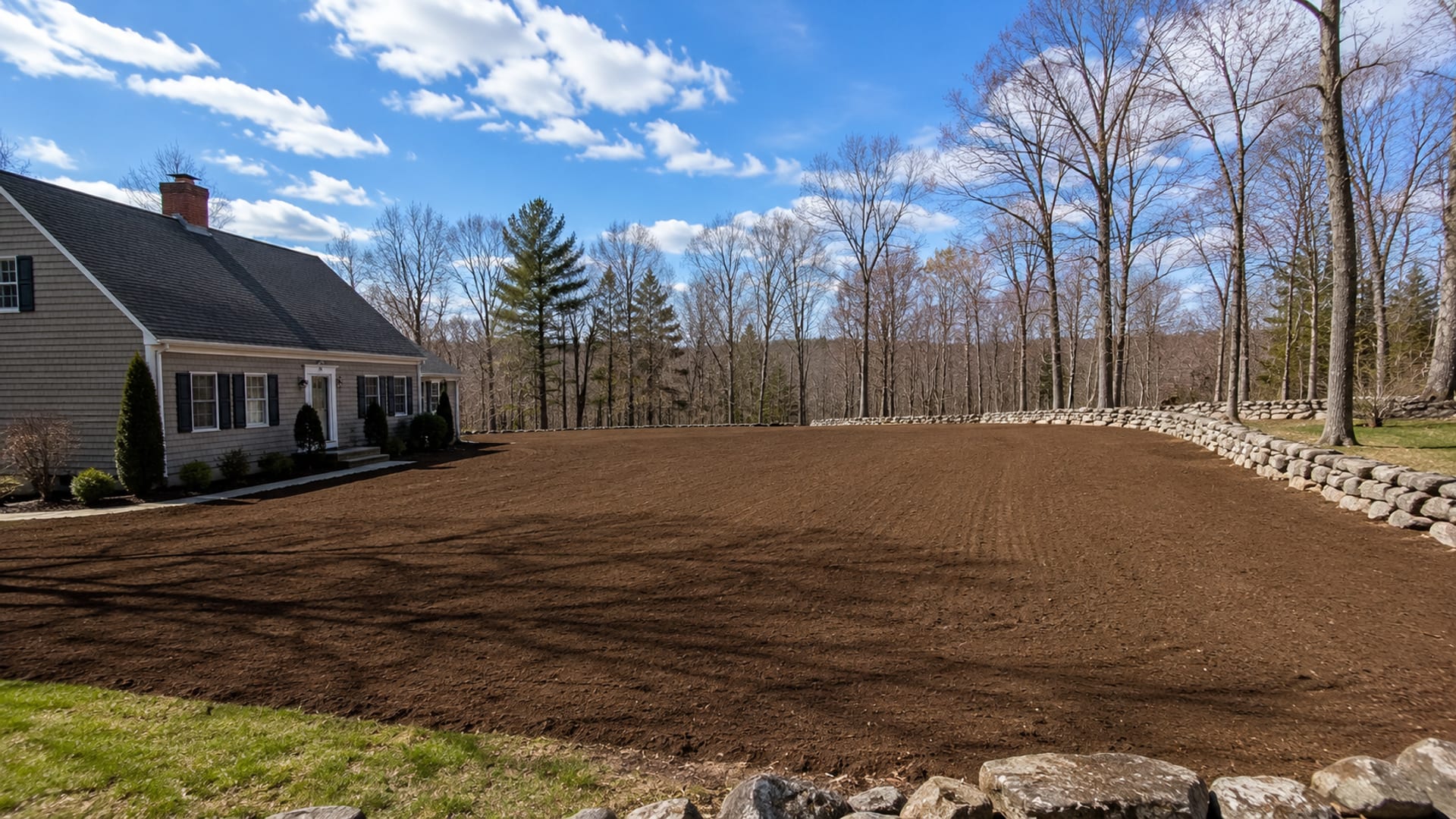 Panoramic view of a fully graded residential property with smooth earth contoured away from a New England home