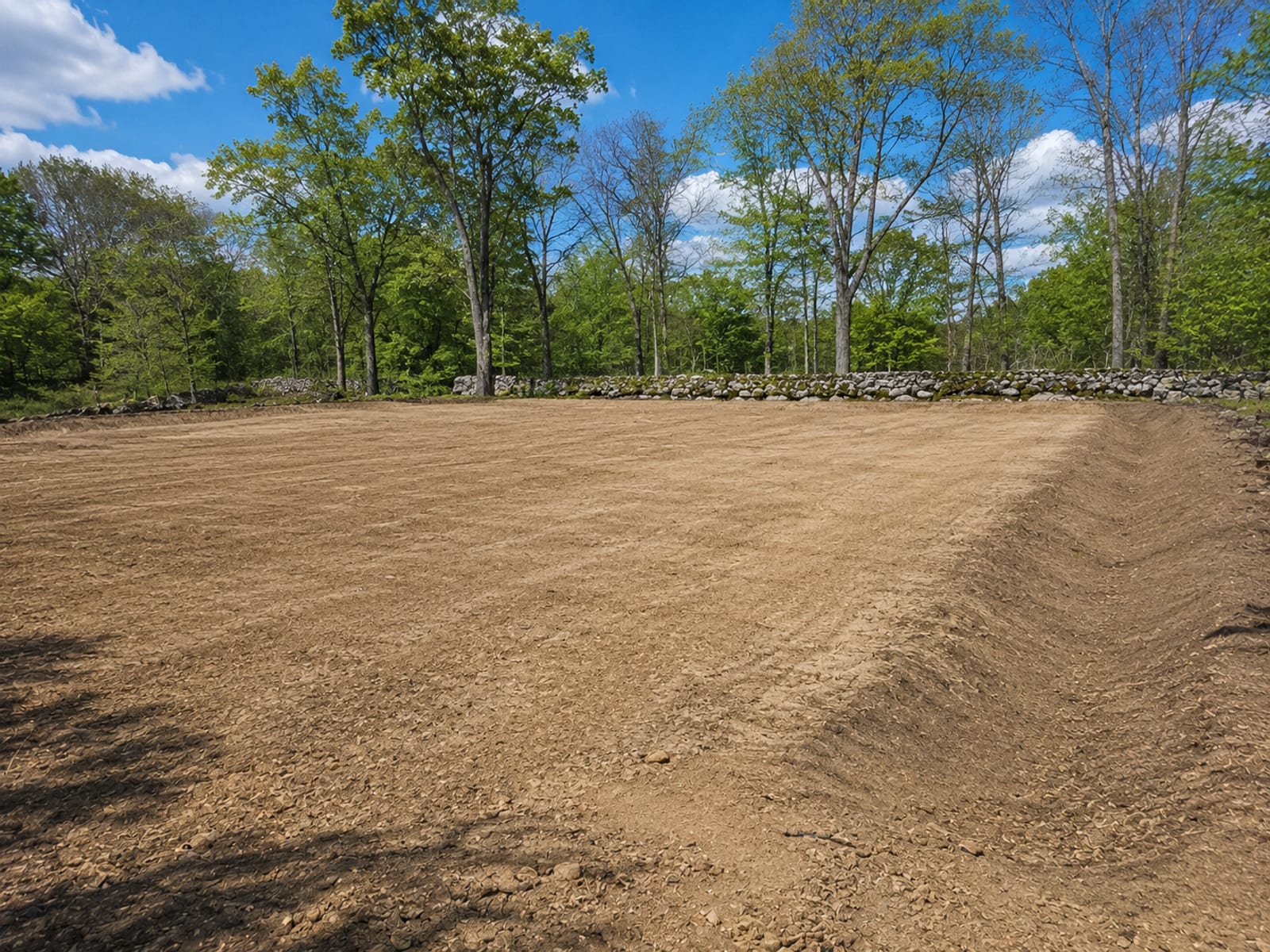 Freshly graded and leveled residential building lot with smooth compacted soil surface and grading swales visible along the perimeter in Connecticut
