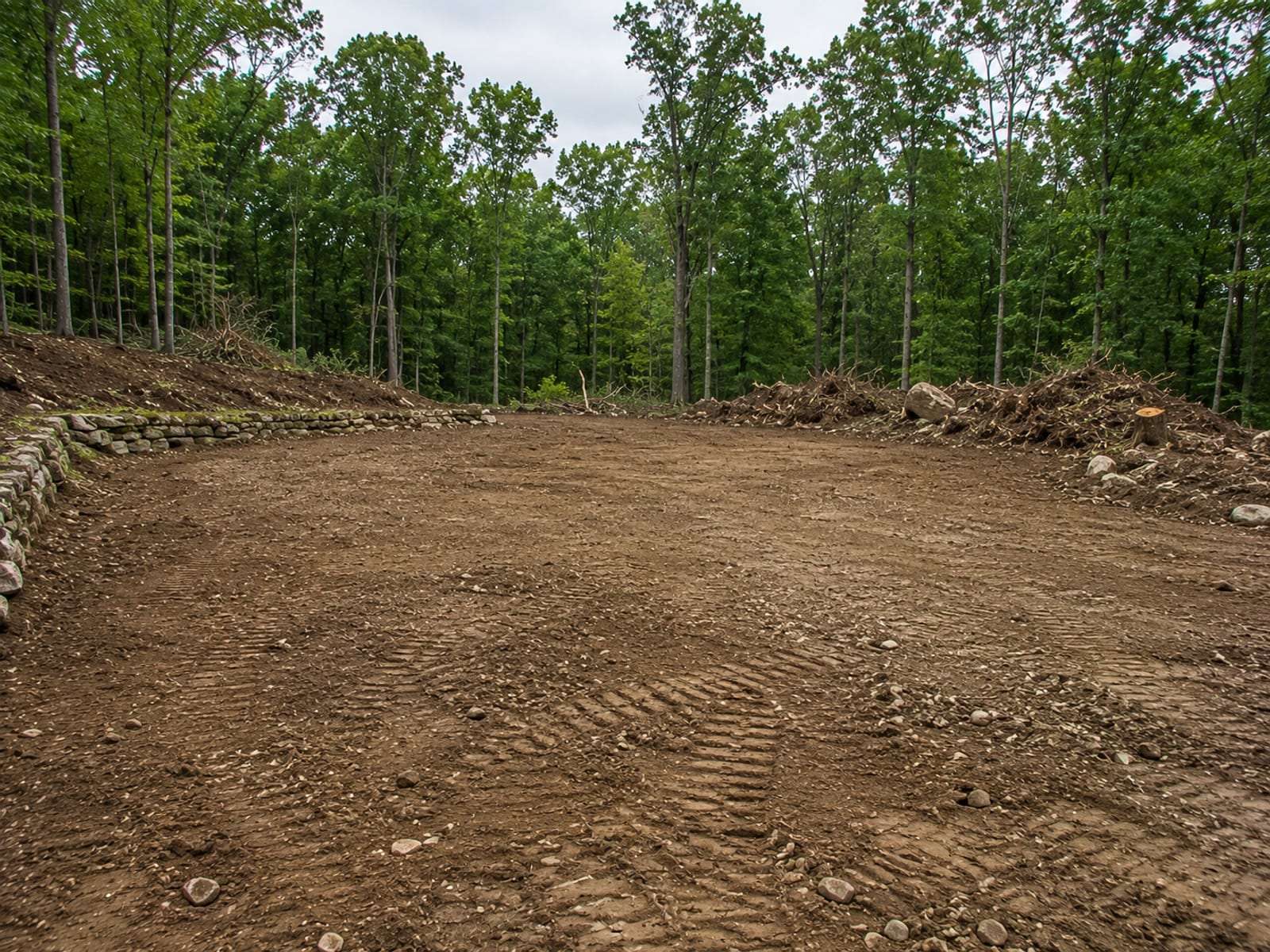 Freshly cleared and rough graded flat building pad on a formerly wooded lot in Oakville CT with stumps and debris piled at the perimeter