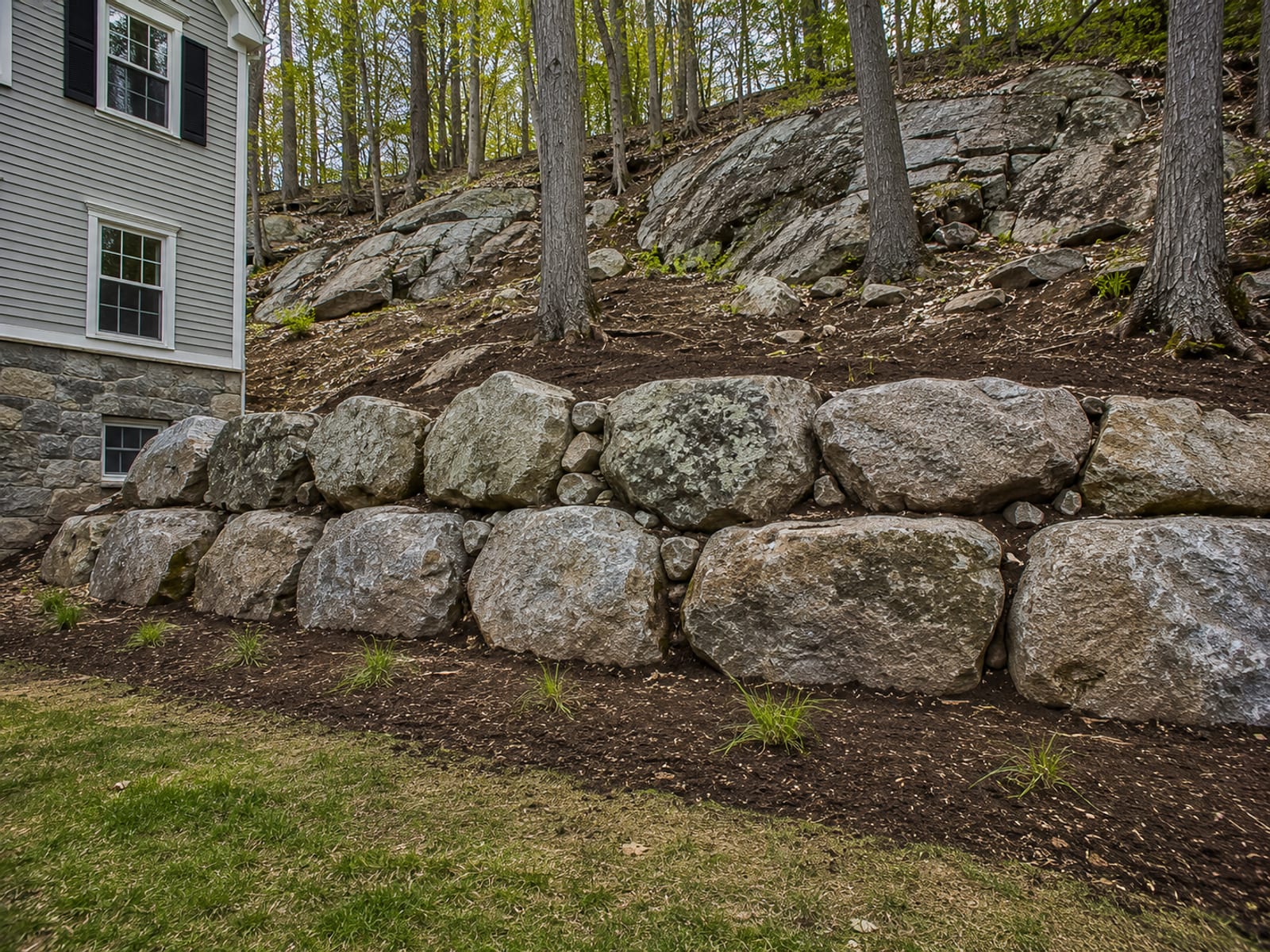 Large natural boulder retaining wall terracing a steep rocky slope beside a Connecticut colonial home