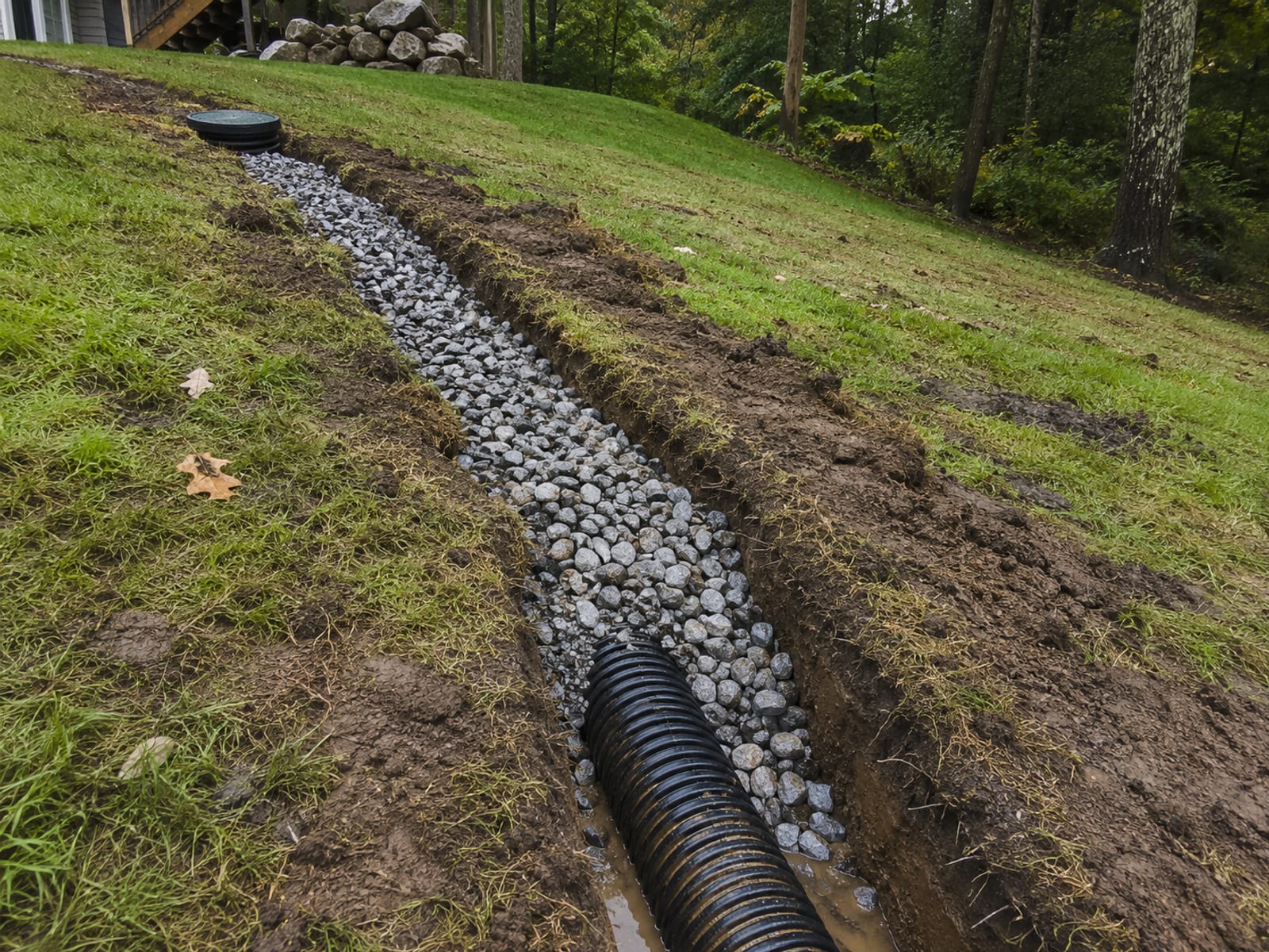 Gravel-filled French drain trench with perforated pipe visible running along a sloped residential yard in Shelton Connecticut