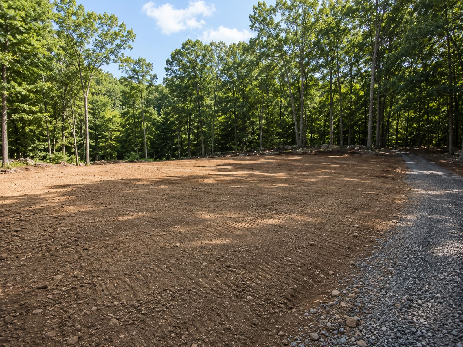 Freshly graded and cleared residential building lot in western Connecticut with exposed glacial till soil and surrounding mature deciduous trees