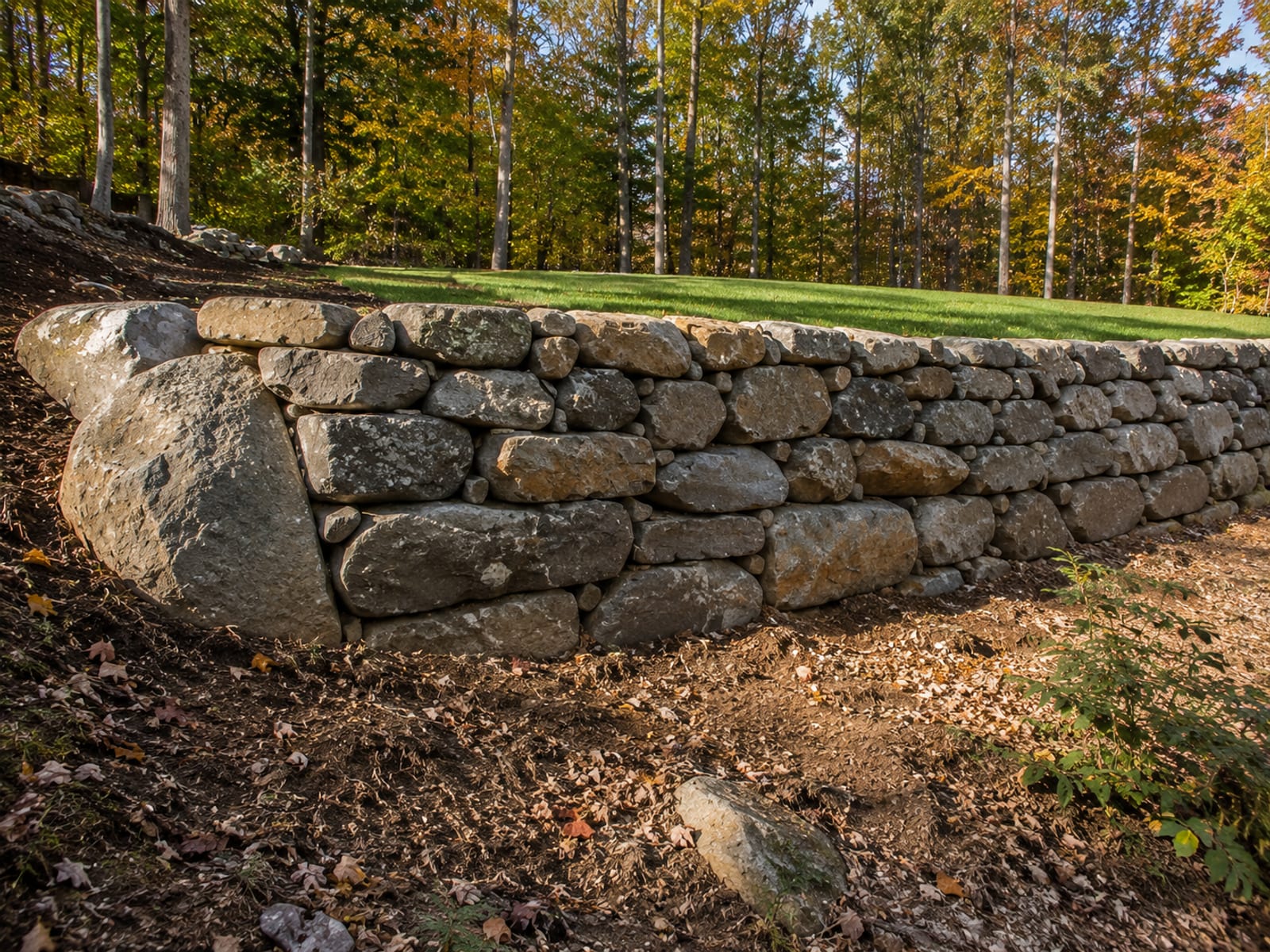 Completed dry-stacked natural stone retaining wall on a sloped residential property in Southbury Connecticut with backfilled level yard above