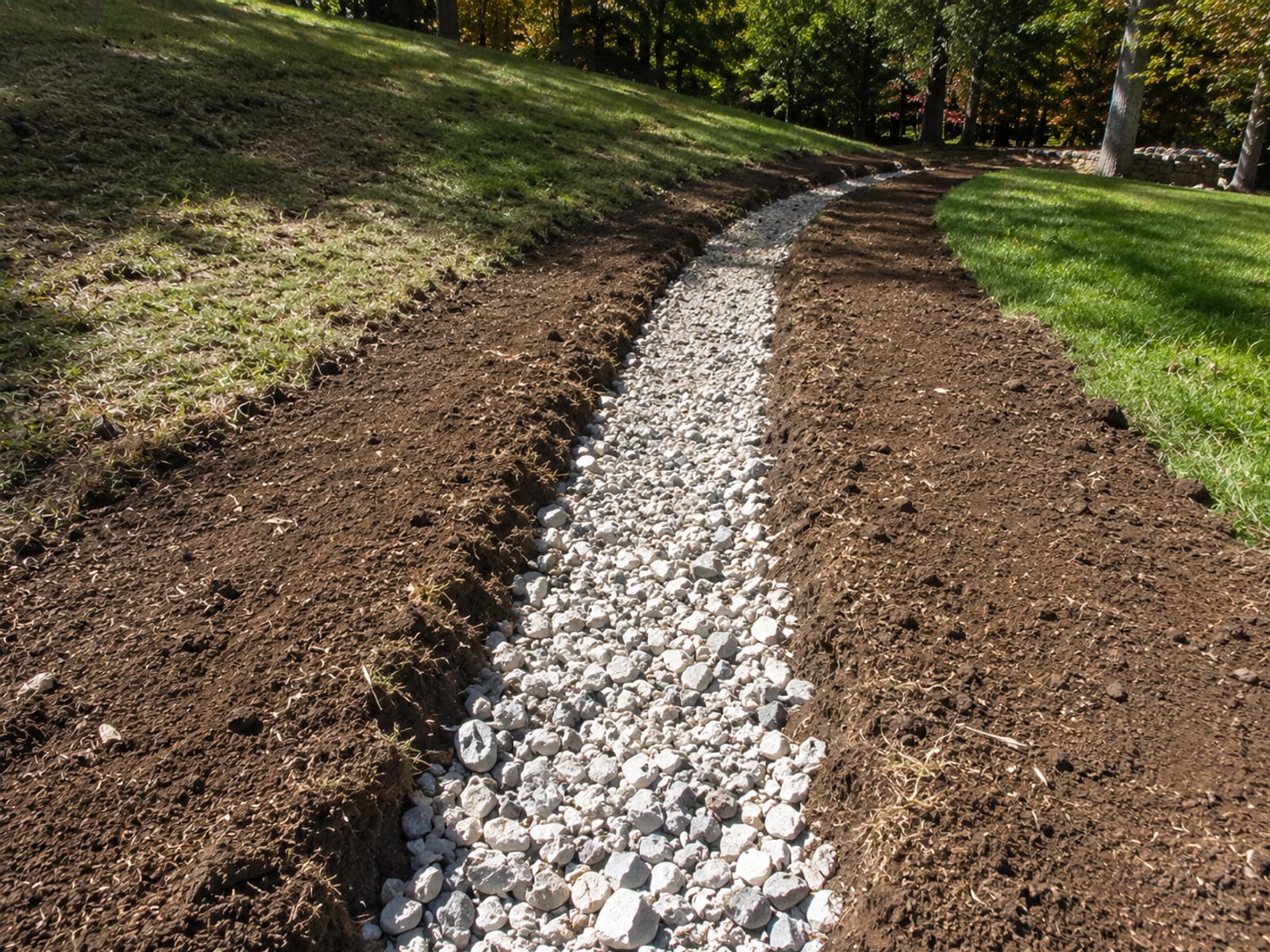 Freshly installed French drain trench filled with clean crushed stone running along a residential yard in Southbury Connecticut