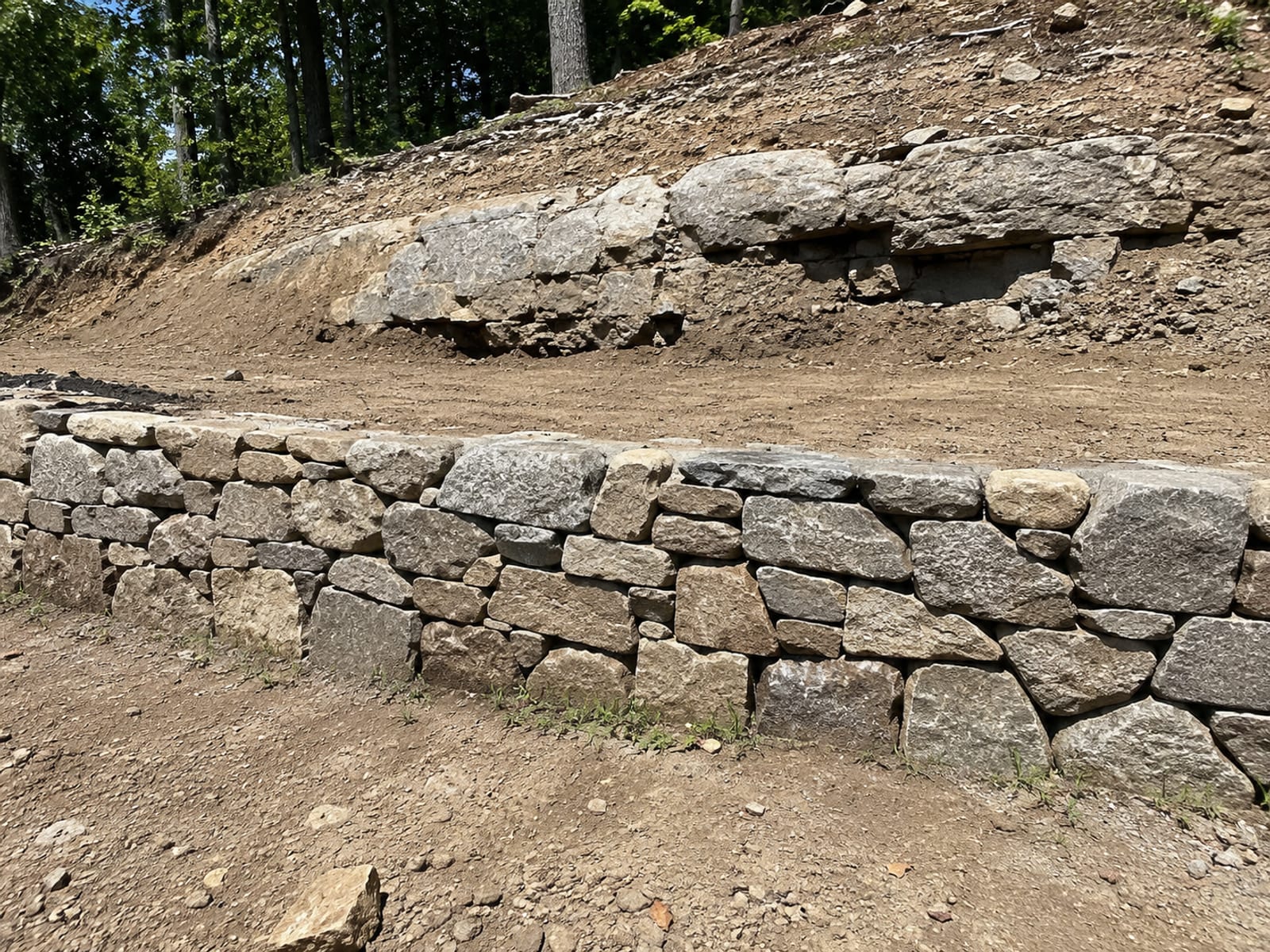 Newly constructed dry-stacked fieldstone retaining wall on a sloped residential lot in Woodbridge CT with exposed ledge rock and graded earth above