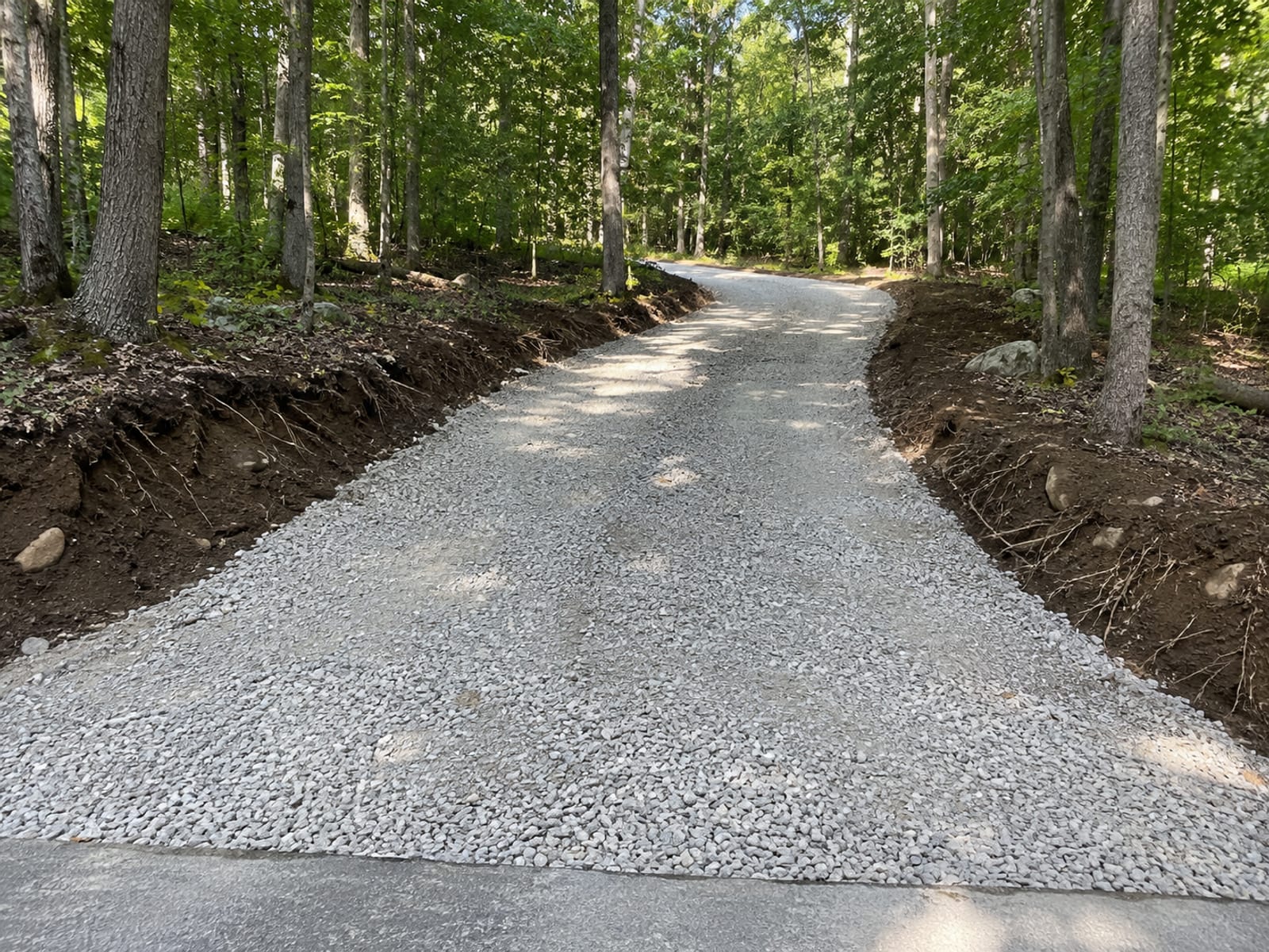 Freshly excavated and gravel-base prepared residential driveway in Woodbridge CT with compacted crushed stone surface and wooded lot on either side
