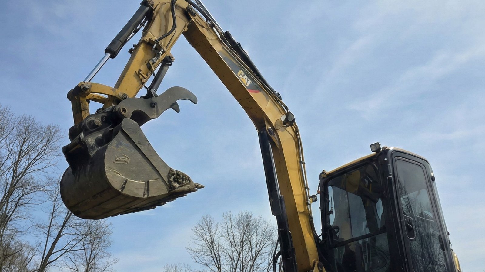 Compact excavator bucket raised during residential excavation work on sloped terrain