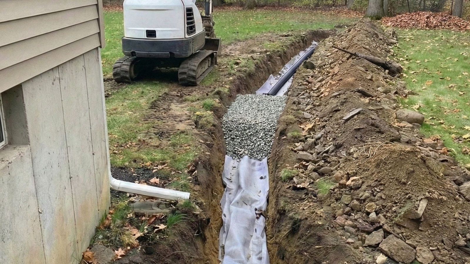 Expert French drain installation with trench, gravel, and pipe beside residential foundation
