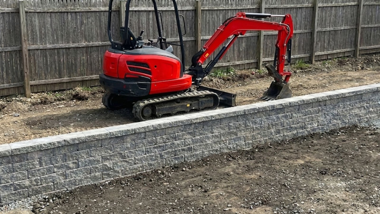 Compact excavator working behind a newly built residential retaining wall